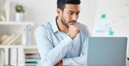 Man sitting in front of laptop with a contemplative facial expression.