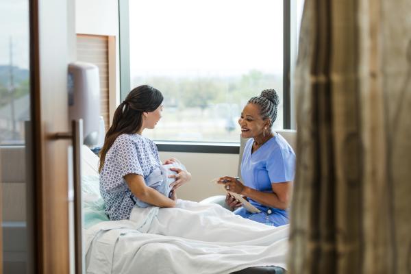 a midwife with a patient who is holding her newborn baby in a hospital setting